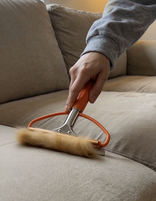 Hand dragging the Nuzzle Fur Remover across couch fabric, lifting fur